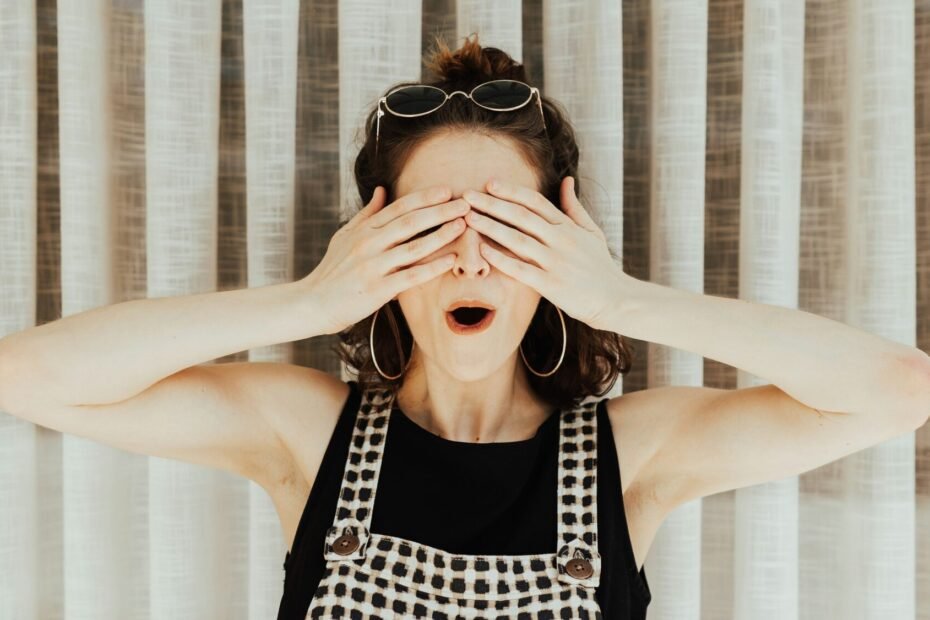 Woman covering her eyes with her hands with her mouth open perhaps in anticipation of a pleasant surprise.